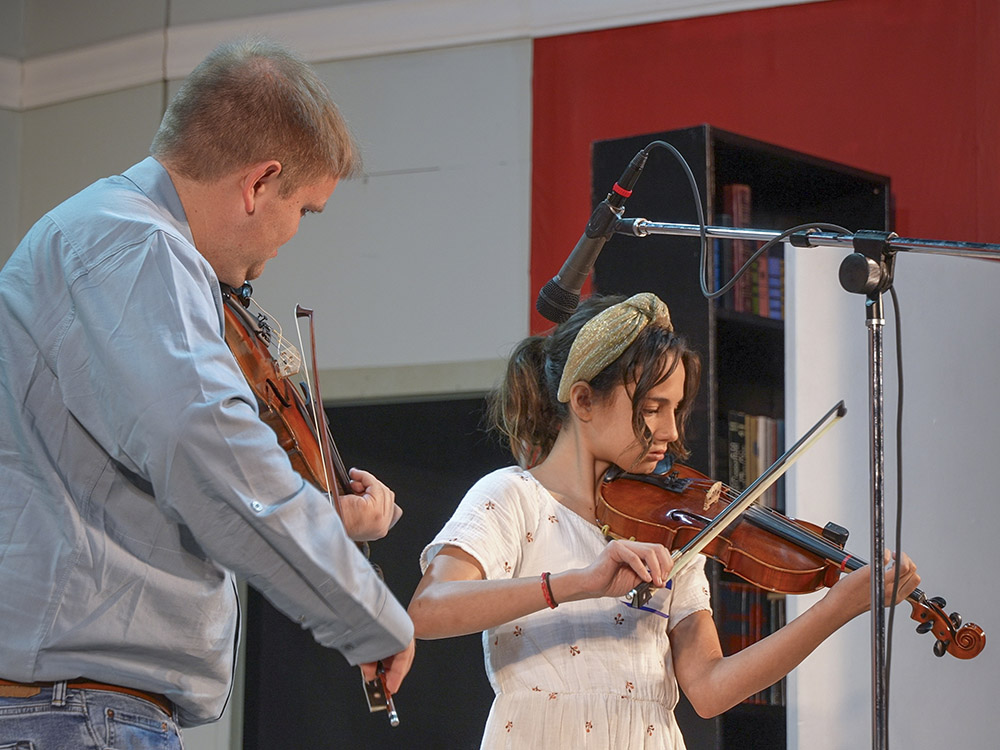 man wearing blue shirt and girl in white dress play Cajun fiddle together
