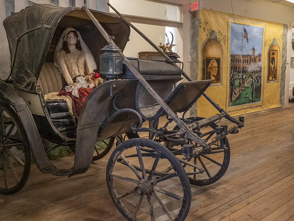 black horse-drawn buggy with model of woman seated inside

