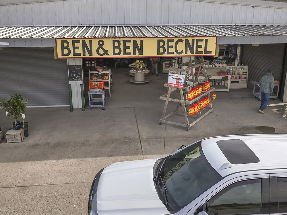 Ben & Ben Becnel sign at fruit stand with vehicle in front of it.