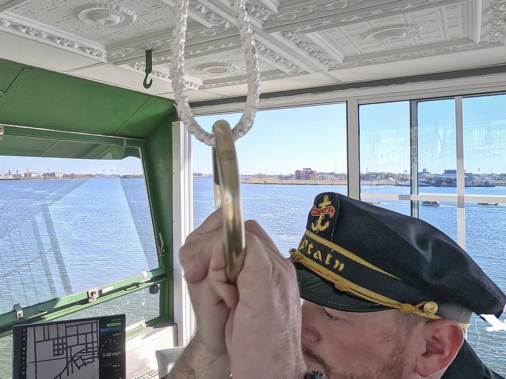 man in black captain hat pulls on brass ring in boat pilot house