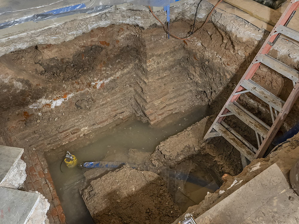 excavation under brick foundation with square hold, ladder and water at bottom of hole
