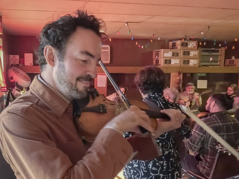 man with dark hair and beard plays fiddle at jam session at Savoy Music Center