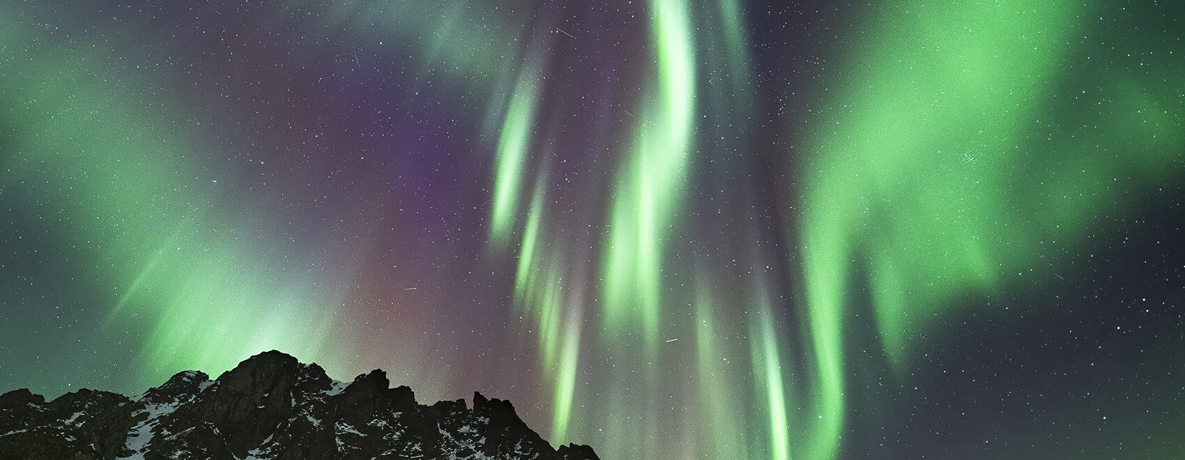 northern lights streaking red white and green above snow capped mountain in norway
