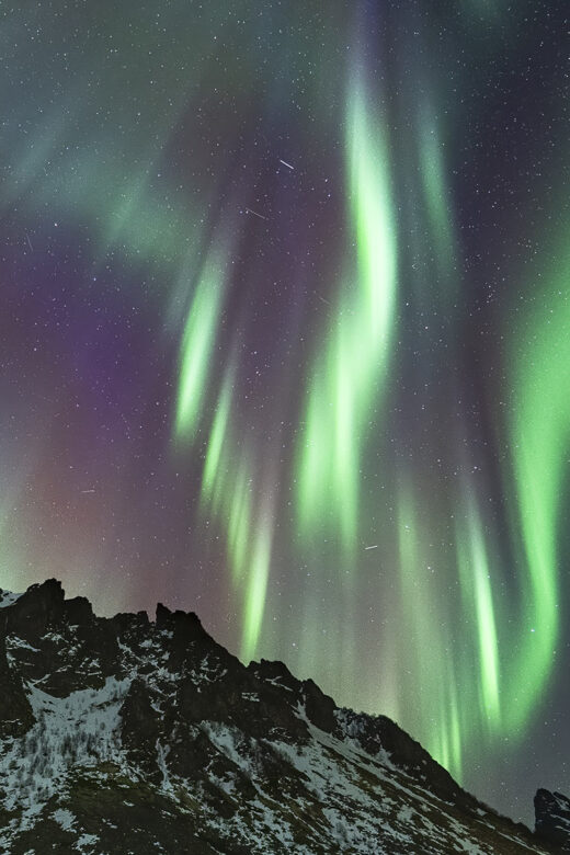 northern lights streaking red white and green above snow capped mountain in norway