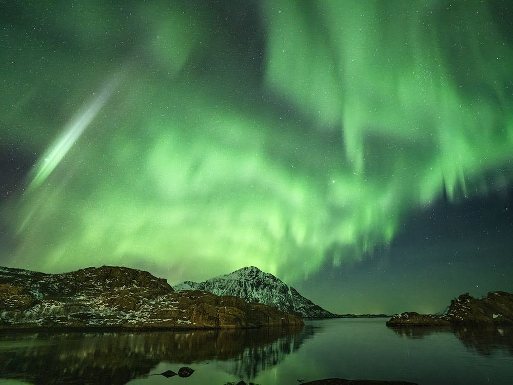 green aurora with streak of white light above mountain and fjord
