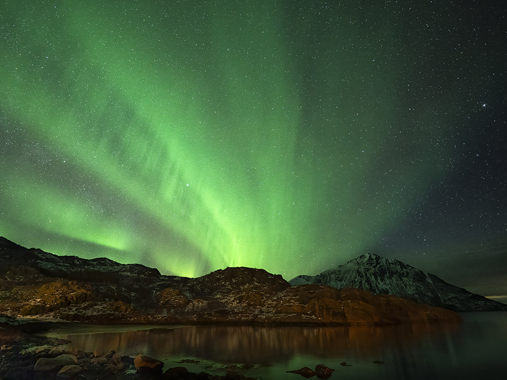 streak of green northern lights above mountains and water
