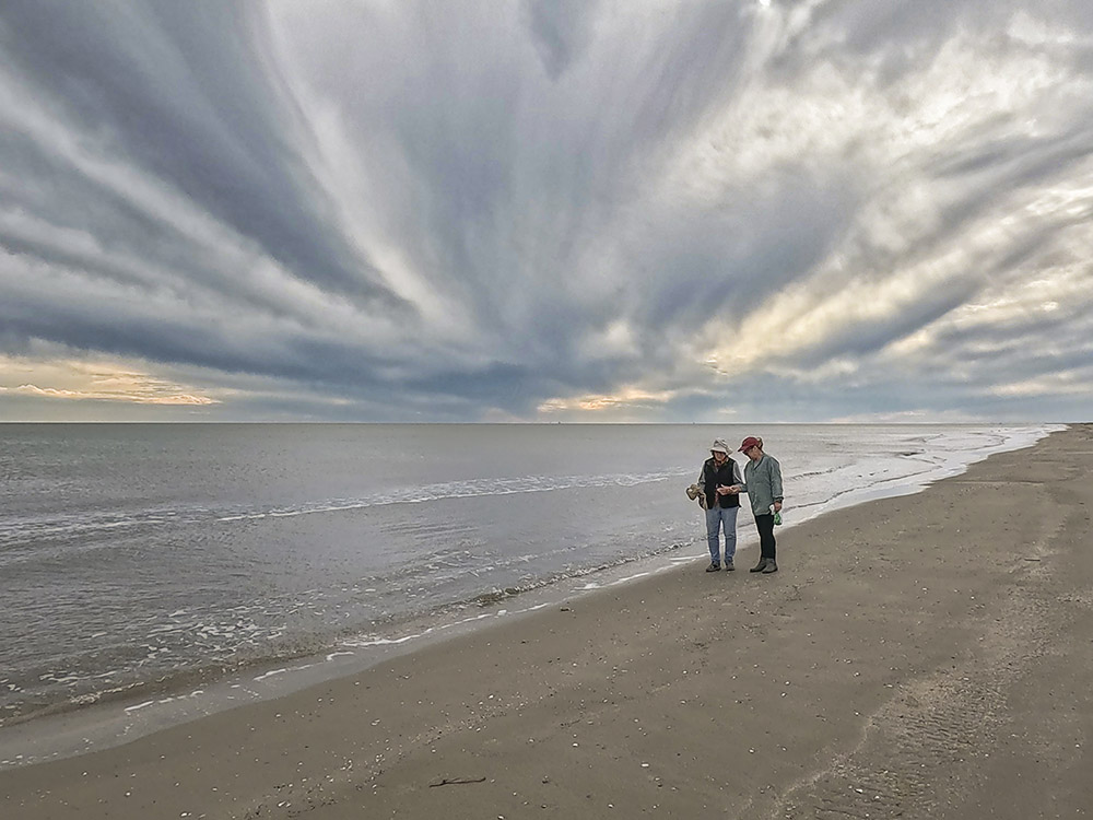 dramatic clouds above two woman on sandy beach at gulf