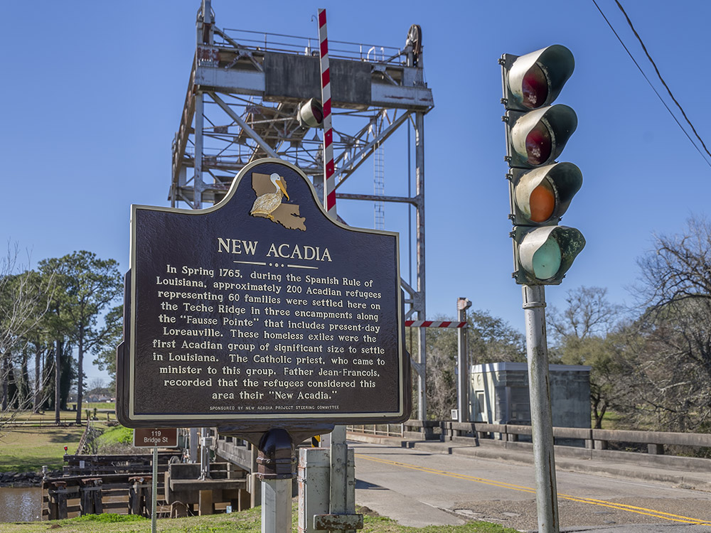 brown historical marker for new acadia near metal drawbridge and traffic signal