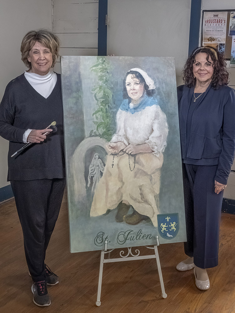 two women stand next to portrait of acadian woman