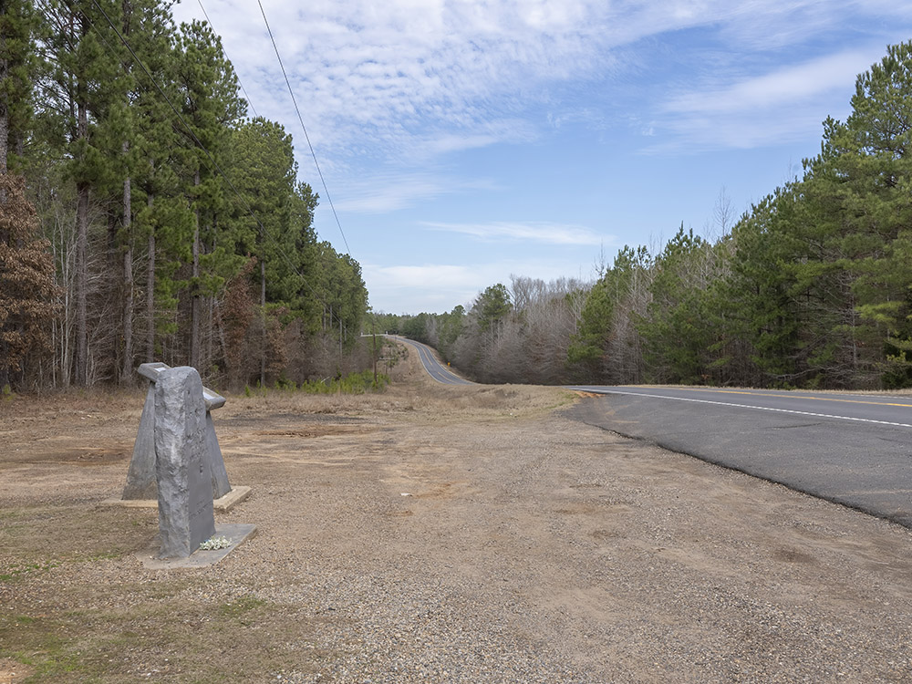 gray monument along highway lined with trees
