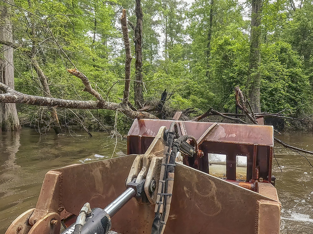 hydraulic metal bucked moves trees out of waterway