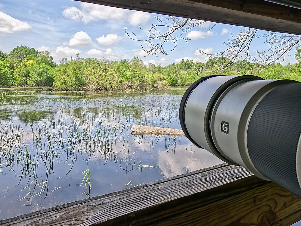 camera lens pointed through window at lake nature scene