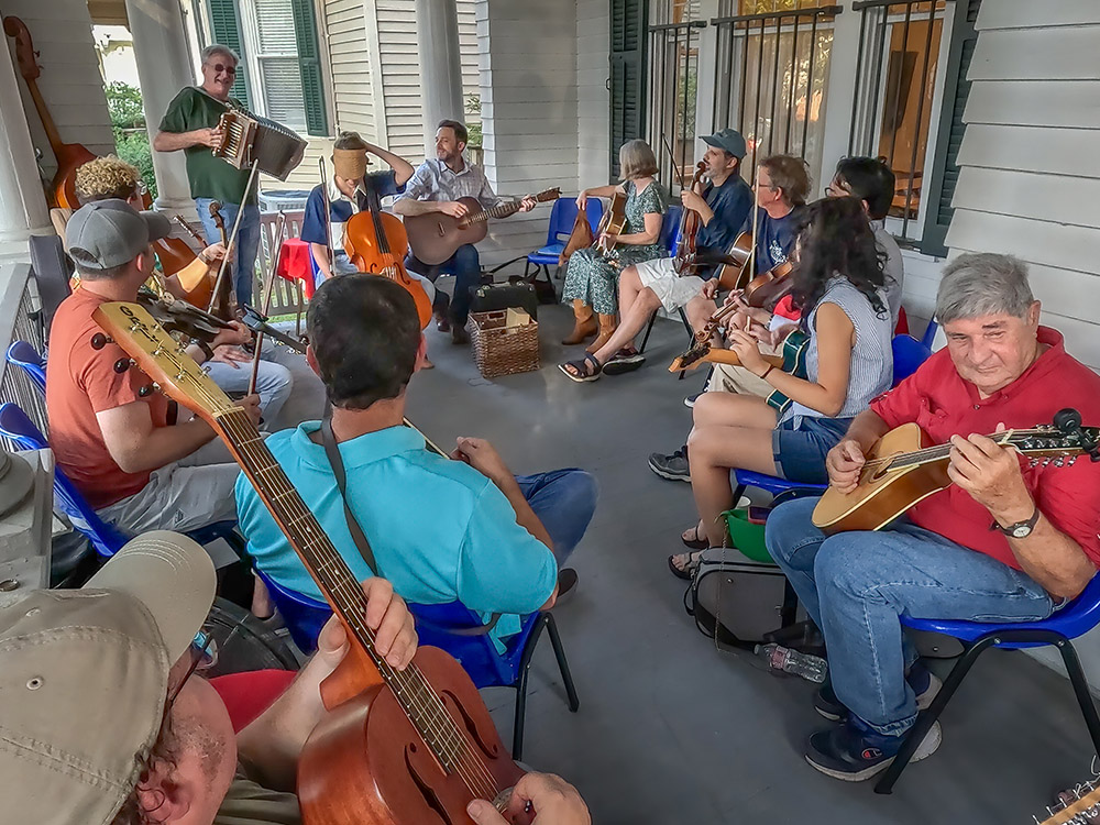 musicians sitting in chairs on front porch playing acoustic instruments in jam session