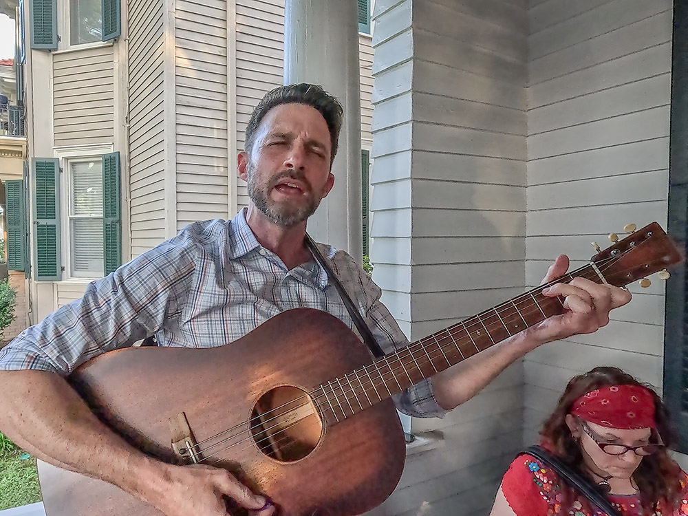 man with dark hair and beard playing guitar and singing