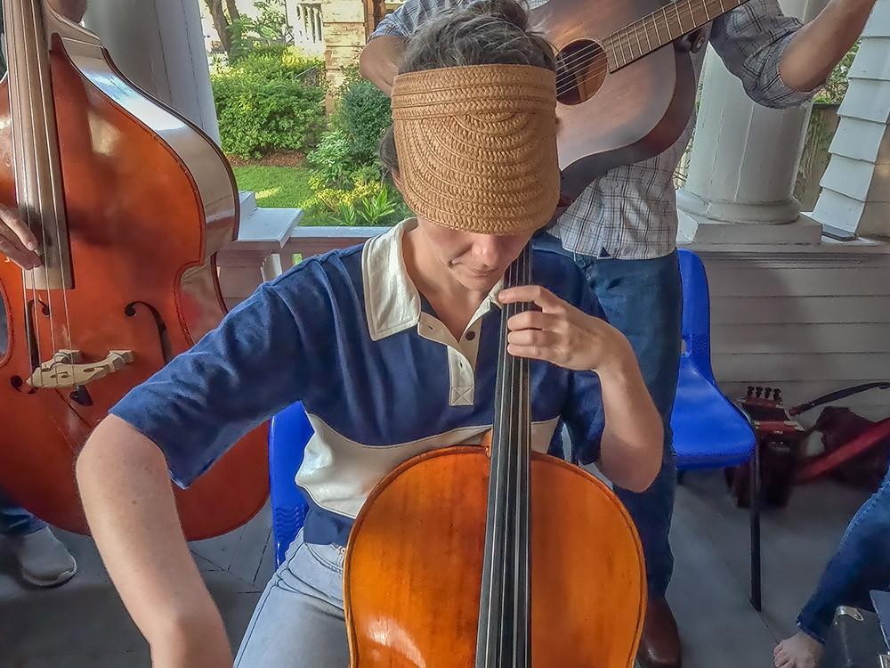 woman in blue and white striped shirt, blue jeans and straw hat plays cello