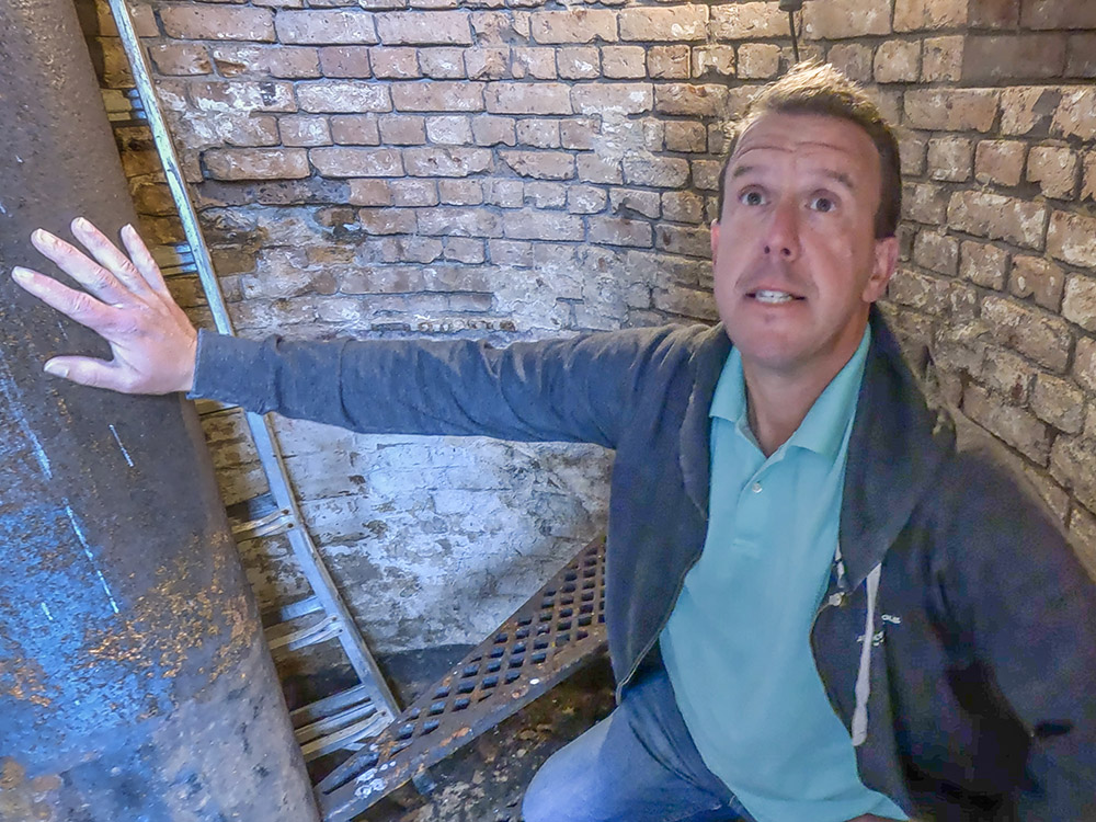 man in blue shirt and blue jeans looks up inside brick lighthouse