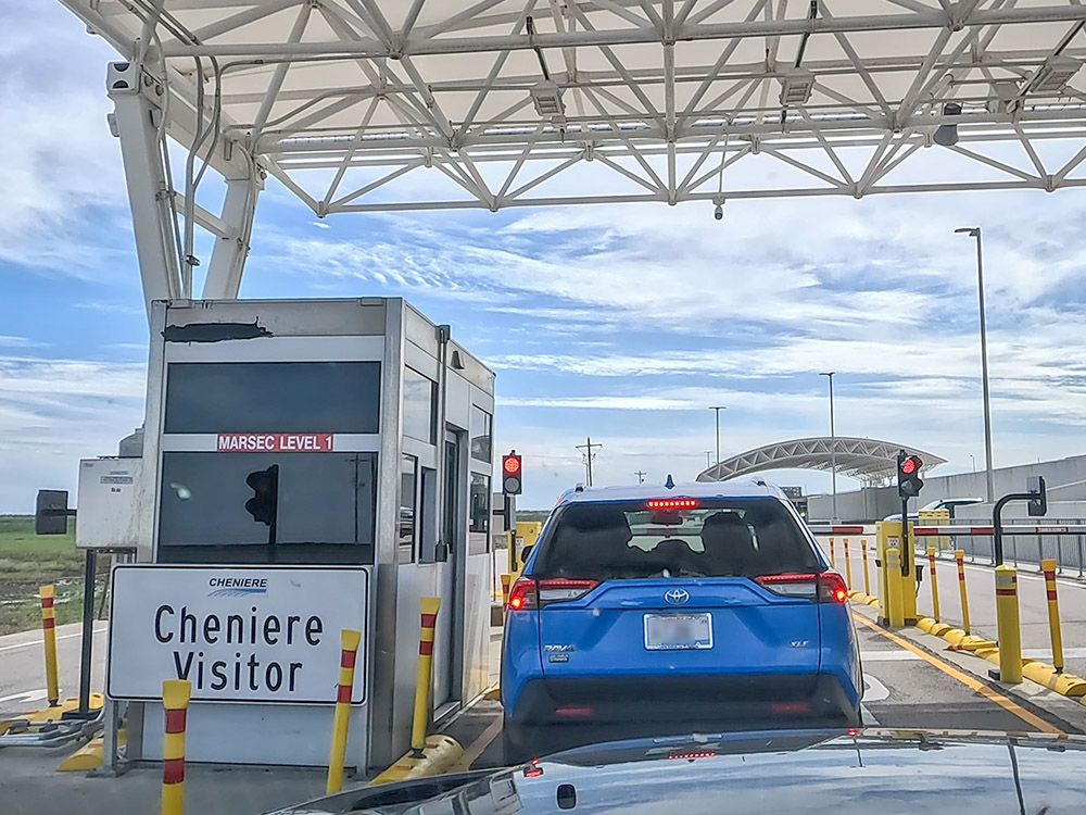 small blue car at entrance gate with sign cheniere visitor