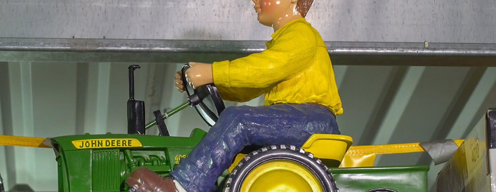 toy tractor with male toy figure in blue pants, yellow shirt and green hat riding tractor