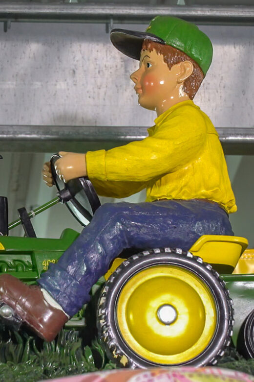 toy tractor with male toy figure in blue pants, yellow shirt and green hat riding tractor