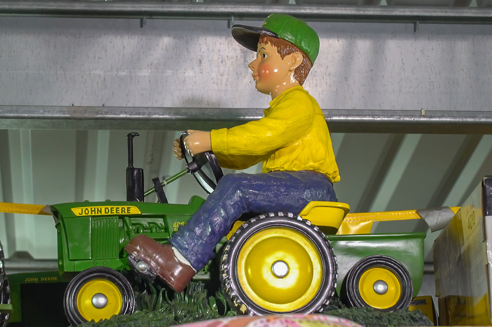 toy tractor with male toy figure in blue pants, yellow shirt and green hat riding tractor