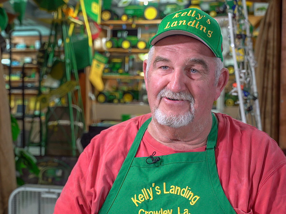 man with green hat and green apron with Kelly's Landing wearing red shirt, gray whiskers