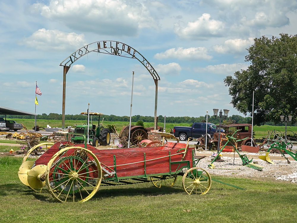 an antique red vehicle with yellow metal wheels in front of welcome side in yard