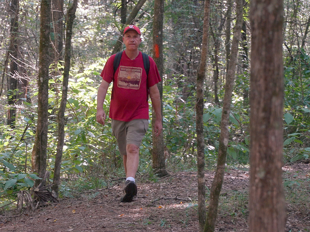 man in shorts, red t-shirt and red cap hiking trail through woods