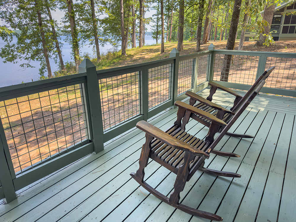 wood rocking chairs on green wood deck overlooking forest and lake