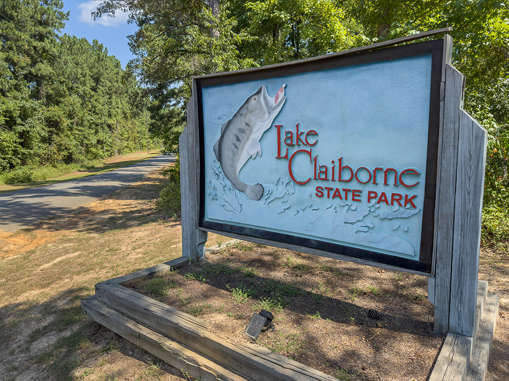 blue sign on road in front of trees with picture of fish and Lake Claiborne State Park