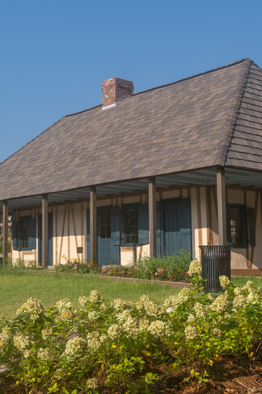 old wood and mud Creole Roque house on sunny day with garden in foreground