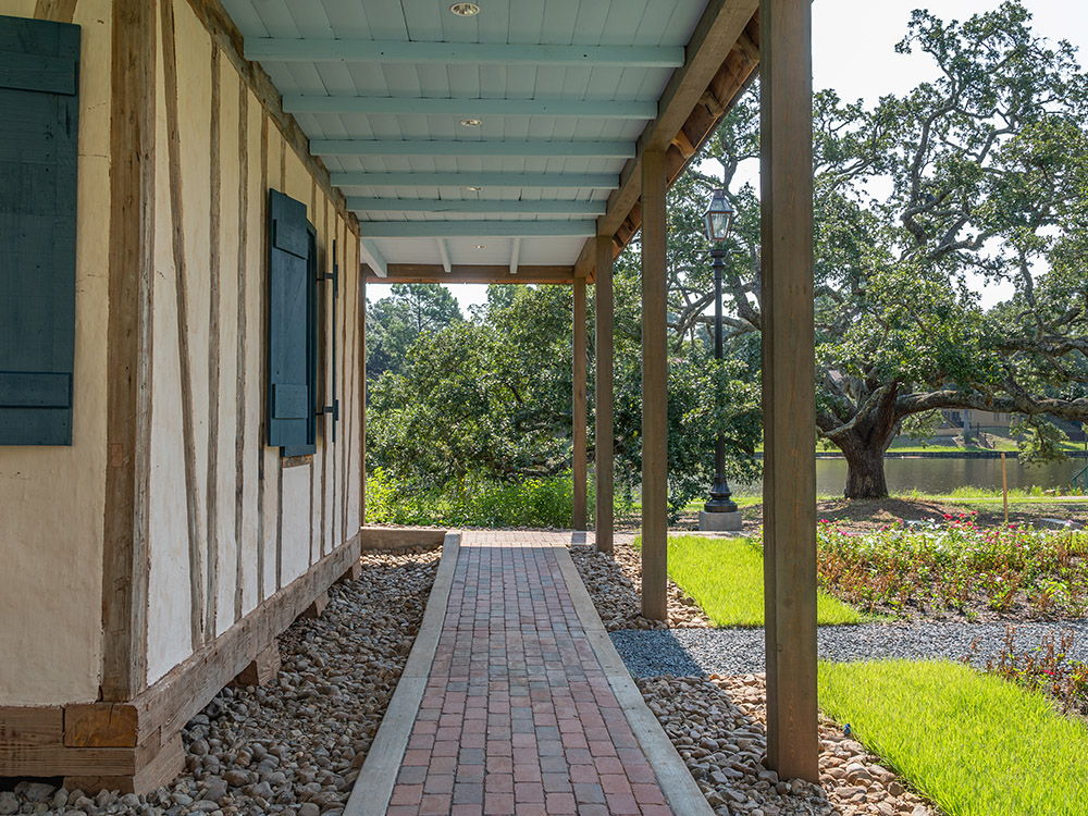 porch of old wood and mud creole house with trees, garden and water in background