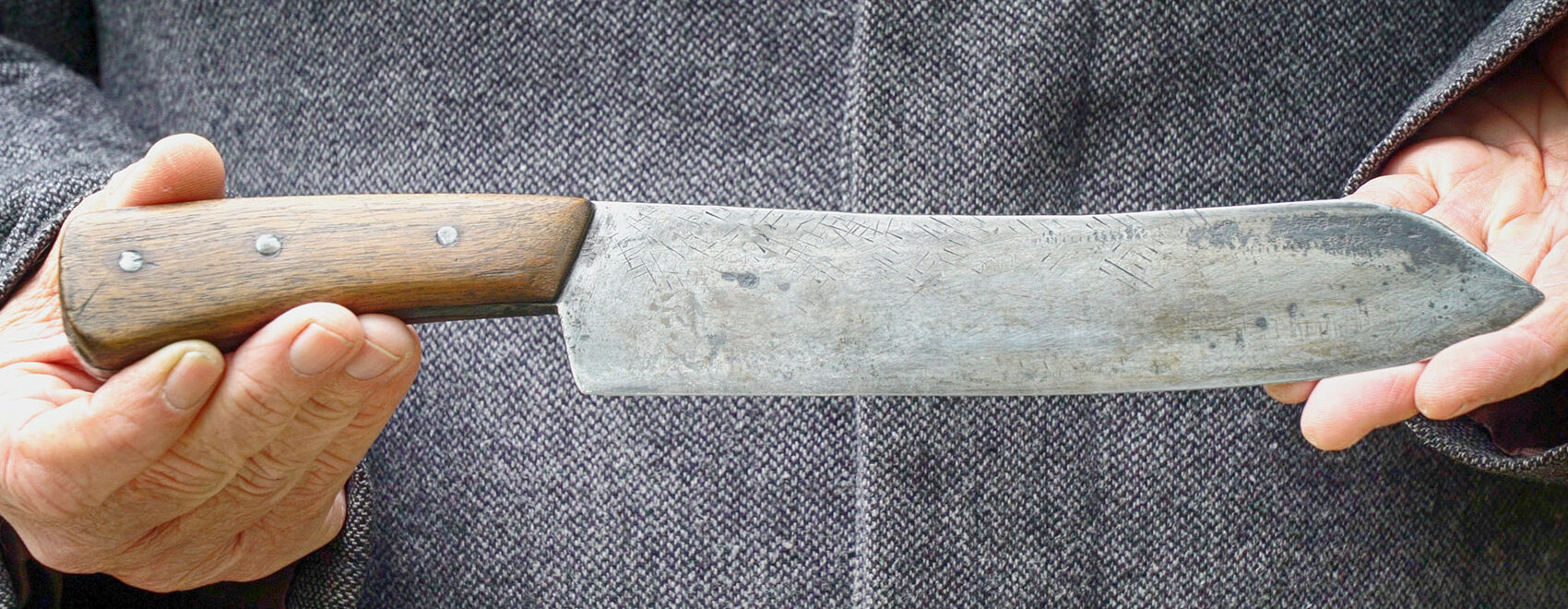 closeup picture of man's hands holding a Bowie knife with brown wood handle and steel blade.