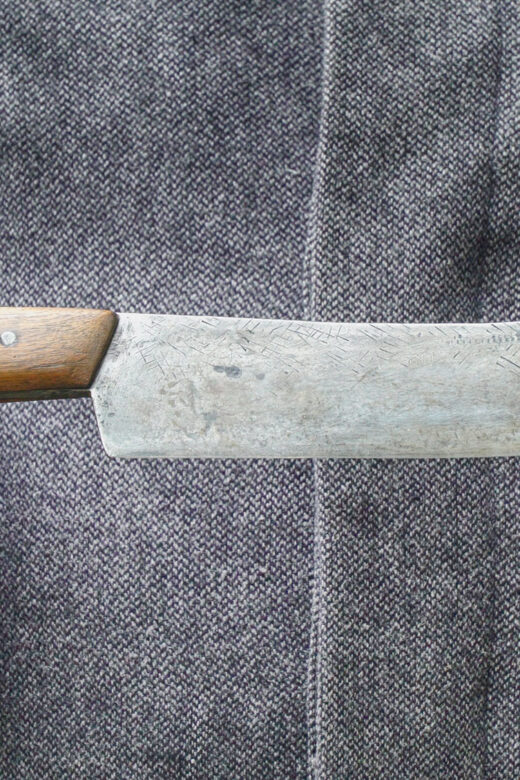 closeup picture of man's hands holding a Bowie knife with brown wood handle and steel blade.