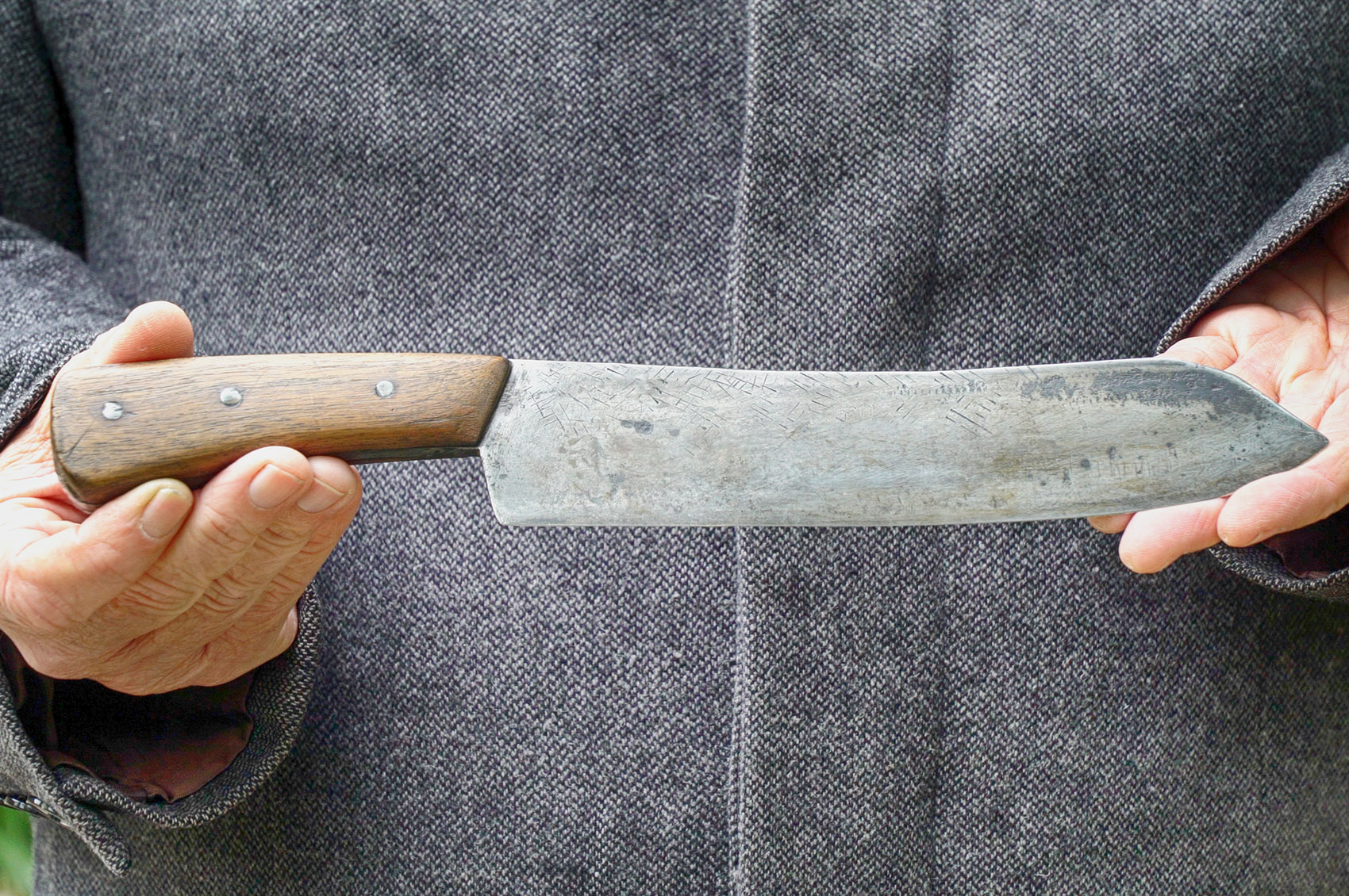 closeup picture of man's hands holding a Bowie knife with brown wood handle and steel blade.