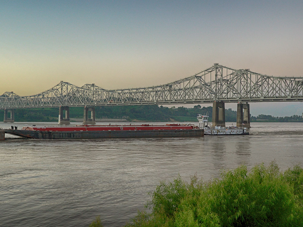 twin steel spans of Mississippi River Bridges with barges and towboat passing underneath