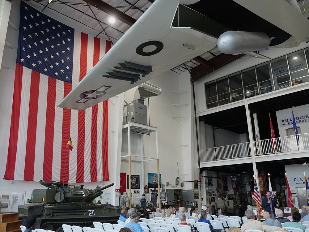 large american flag hangs on wall with display of military vehicles and aircraft