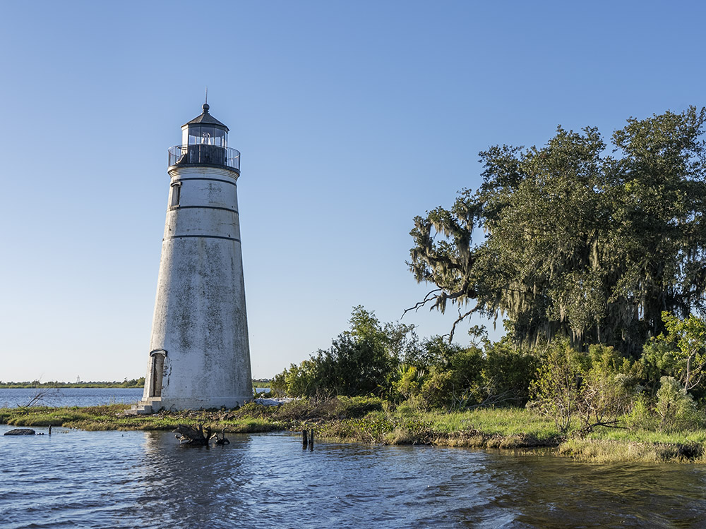 white round lighthouse on the edge of water near trees on sunny day