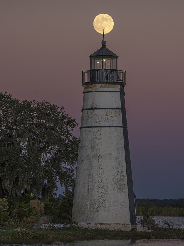 supermoon behind point of lighthouse at twilight