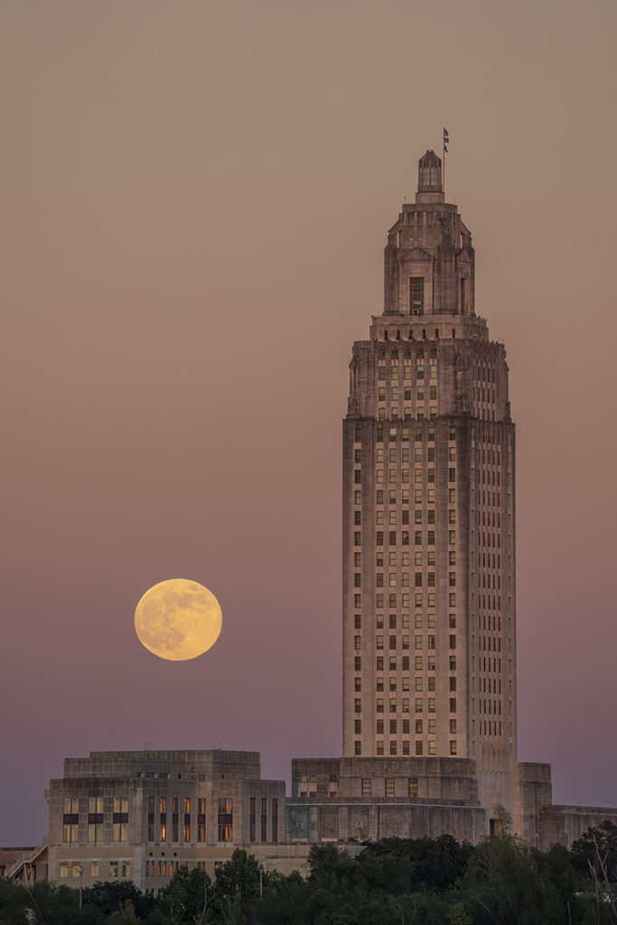 rising full moon with Louisiana state capitol at dusk