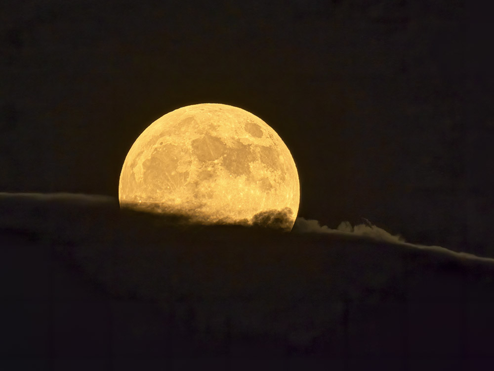 supermoon moving above clouds in dark sky