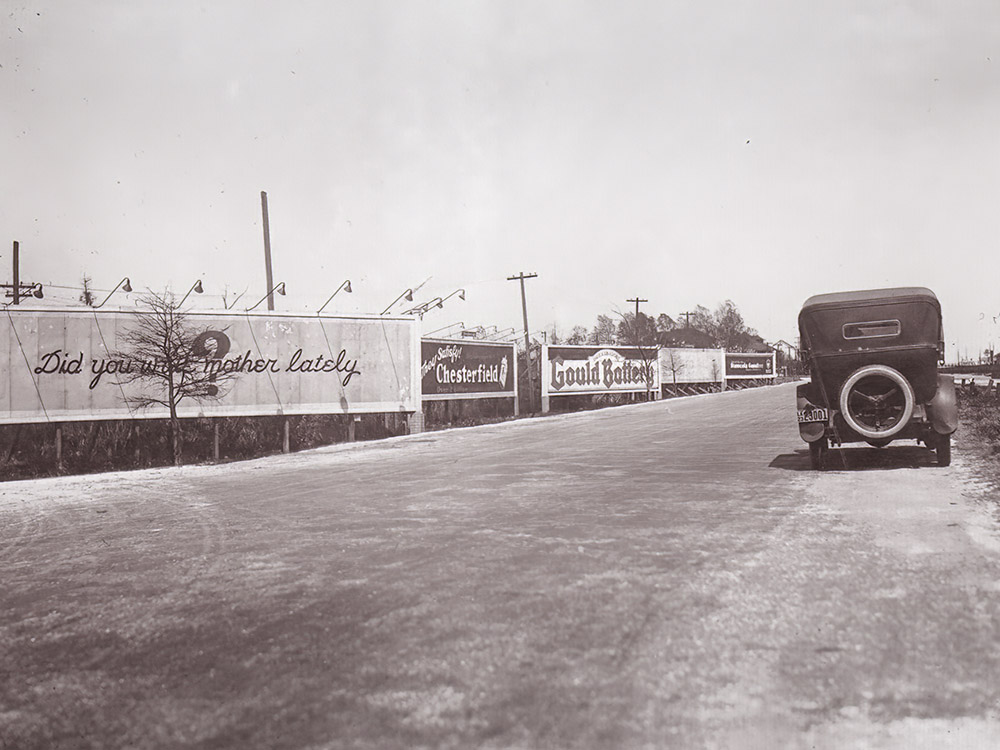 old black and white photo with vintage car and billboards along Jefferson Highway