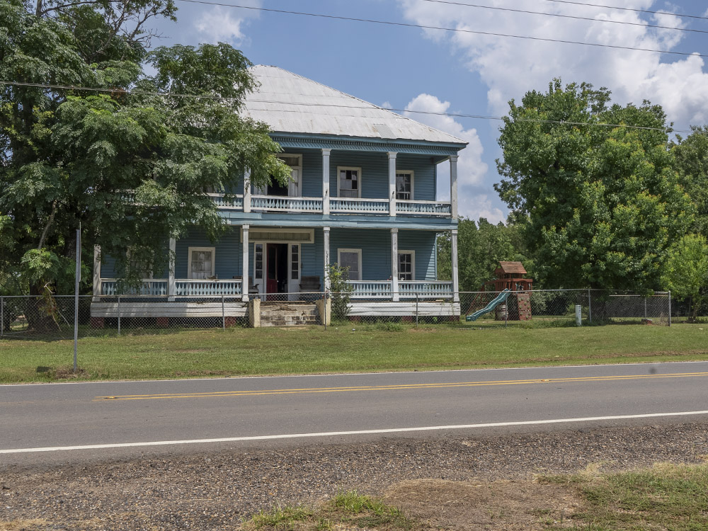 two story old blue house with white railings and posts with white roof along highway