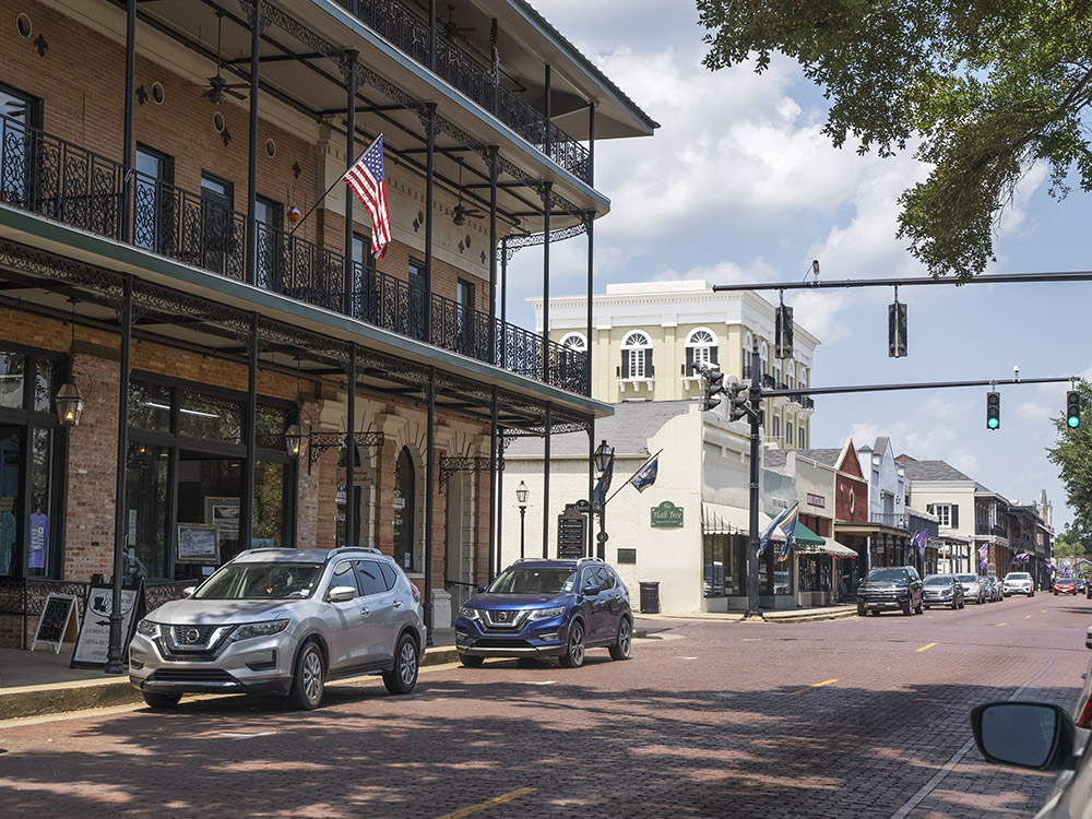 downtown street with traffic signal and parked cars in front of 2 story red brick building