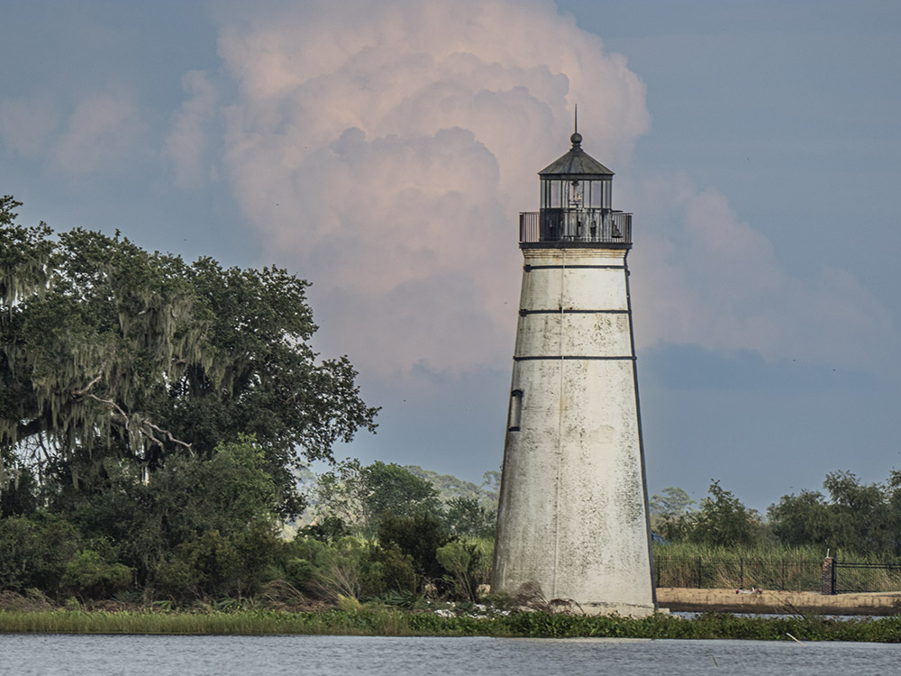 lighthouse and trees near water with pink clouds in sky