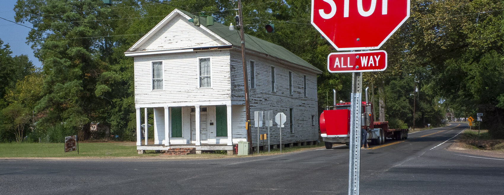 old 2-story white building on street corner with stop sign in foreground