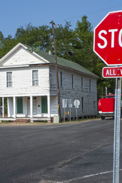 old 2-story white building on street corner with stop sign in foreground