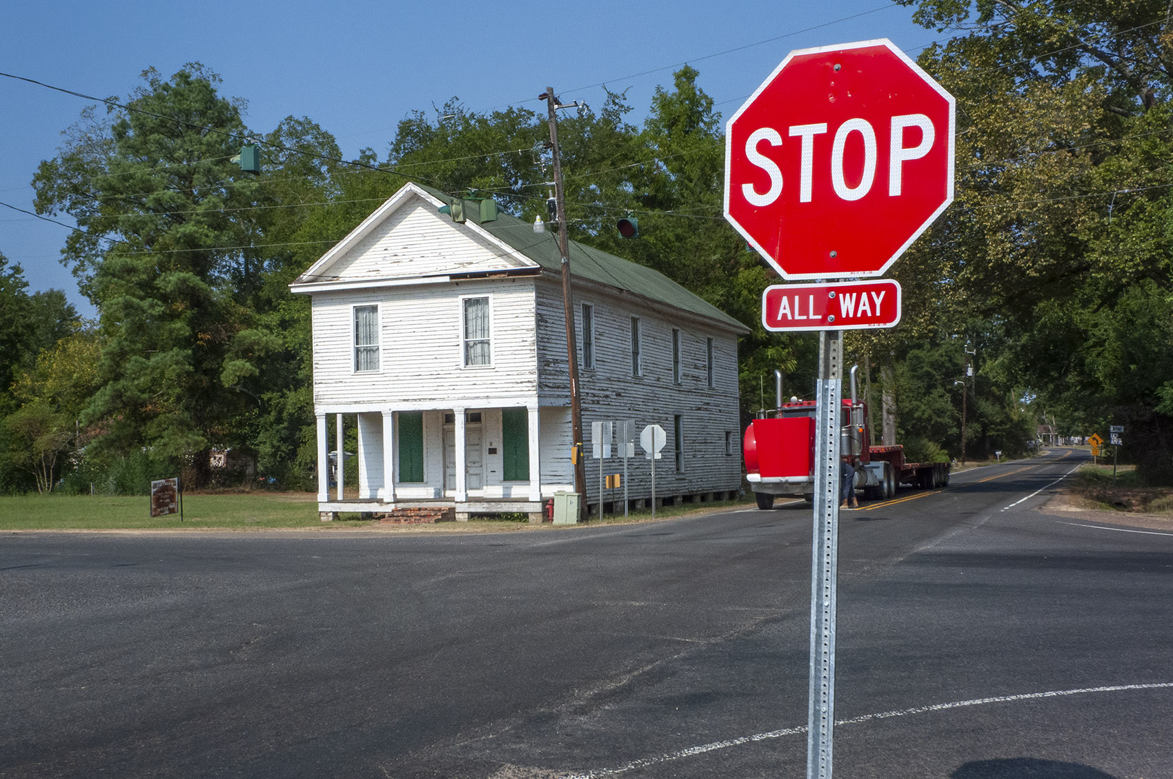 old 2-story white building on street corner with stop sign in foreground