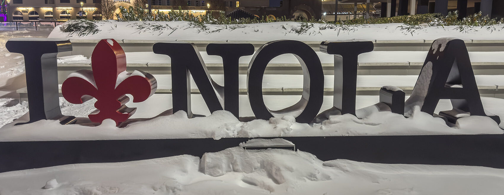 A black and read sign with letters I NOLA and red fleur de lis showing heaving snow in New Orleans