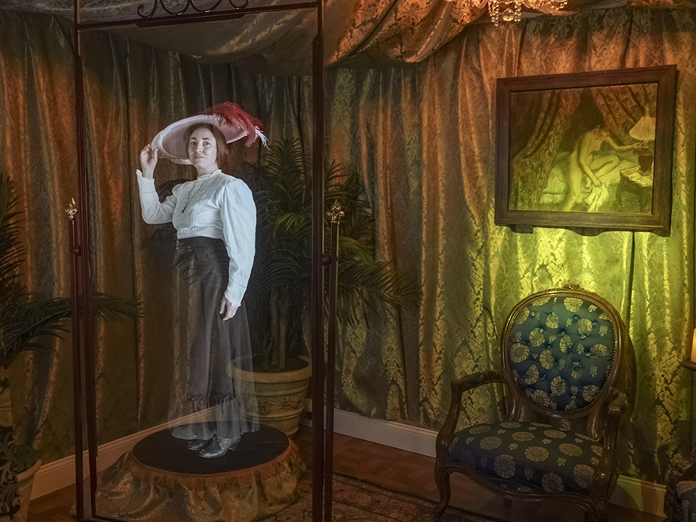 hologram of woman wearing white shirt dark skirt and large hat in parlor of Storyville museum display