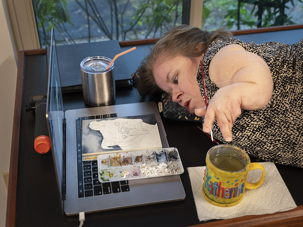 woman artist with watercolors lying next to computer and painting